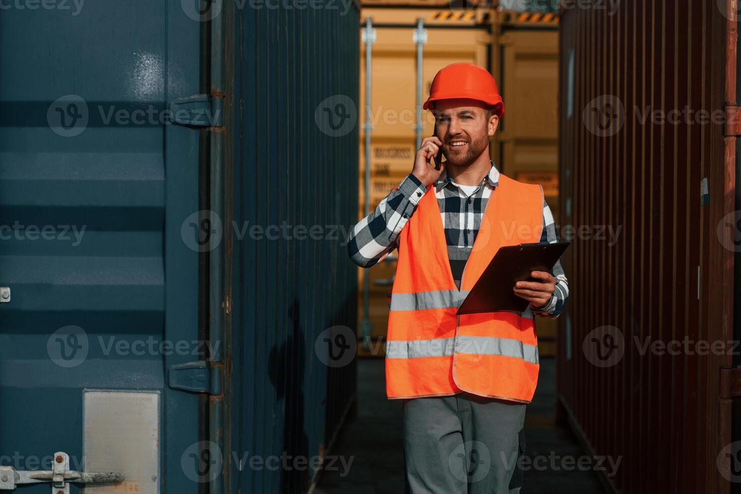 Using phone and ,holding tablet. Male worker is on the location with containers photo