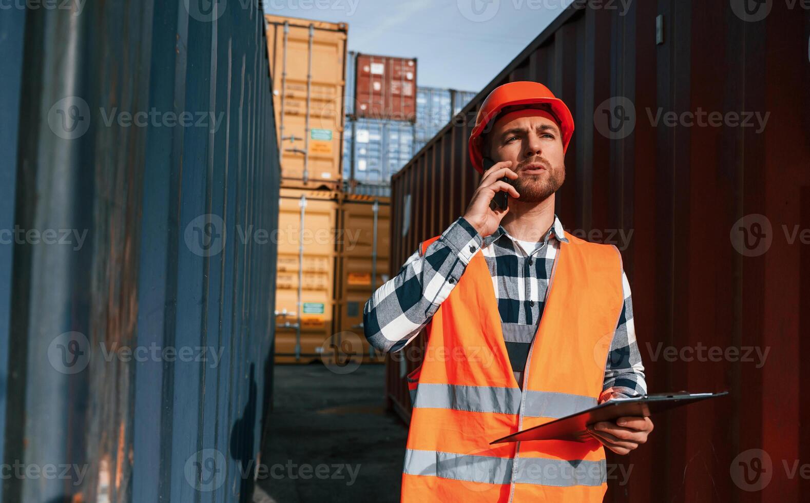 Having, conversation by phone. Male worker is on the location with containers photo
