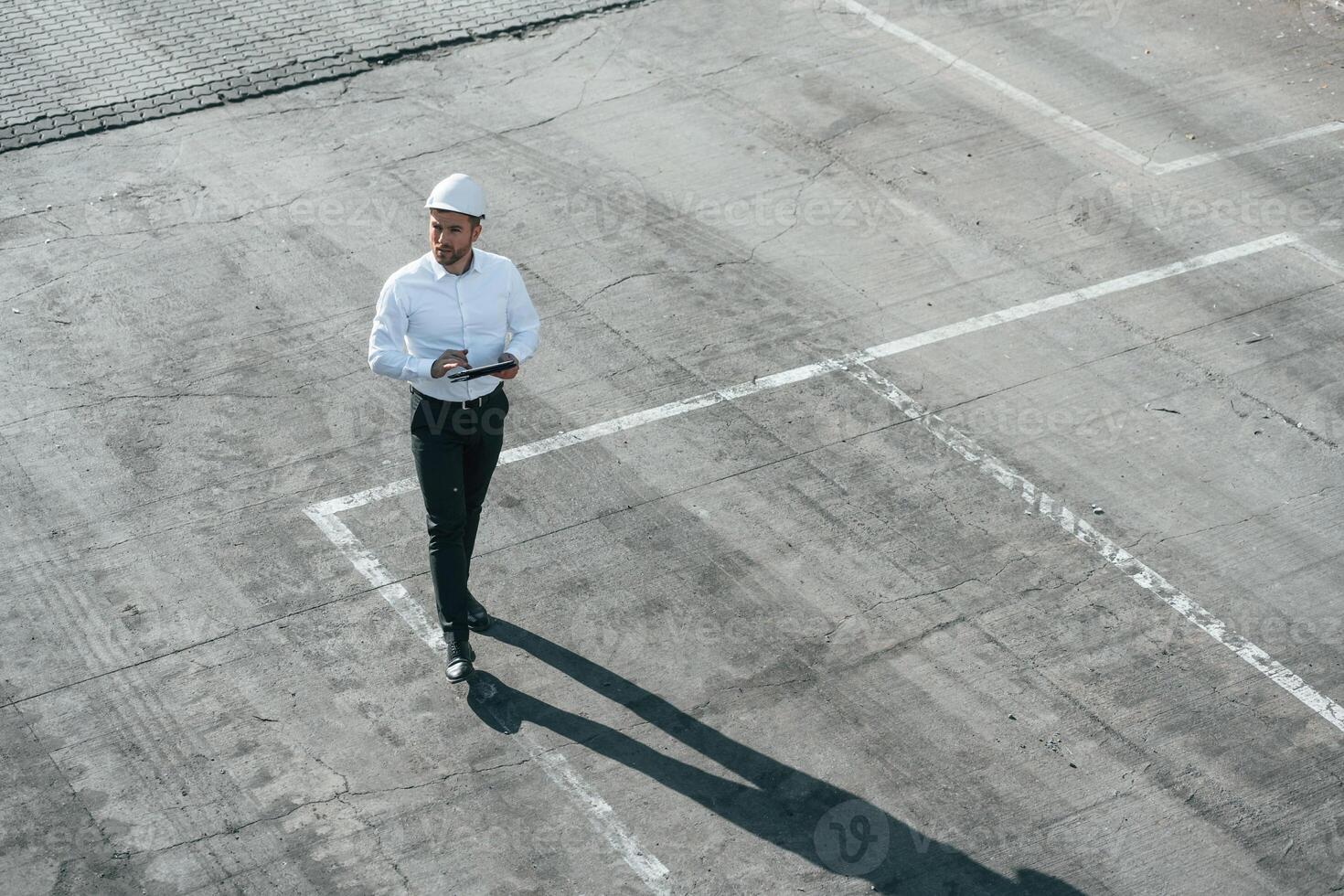 Top view of man in formal clothes and in white hard, hat that is walking with tablet in hands photo