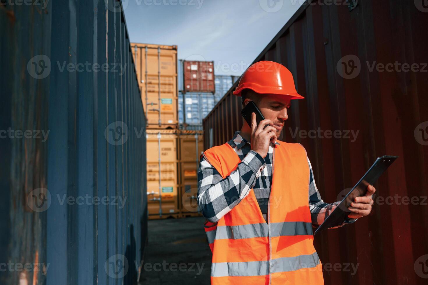Having conversation by phone. Male worker is on the location with containers photo