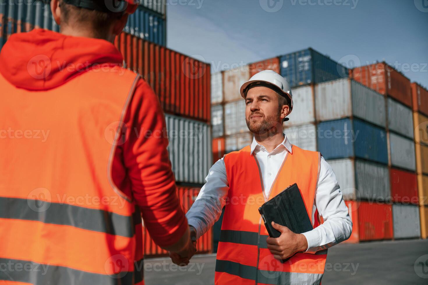 Greetings, handshake. Two male workers is on the location with containers photo