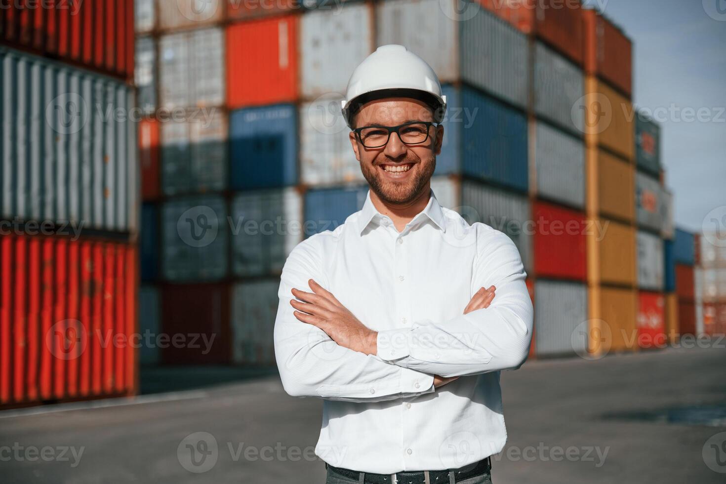 Standing ,with arms crossed.. Male worker is on the location with containers photo