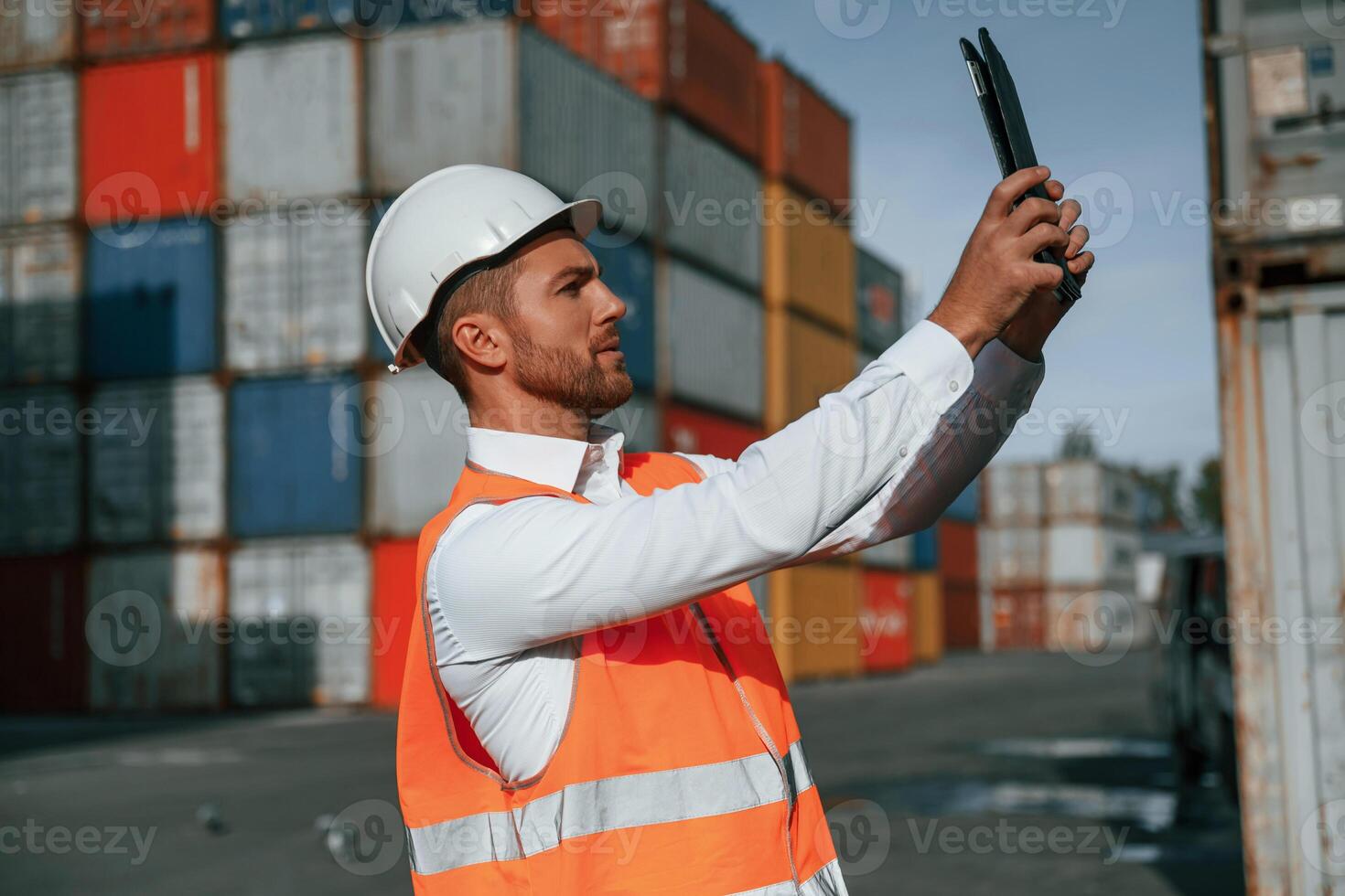 Taking photos by using tablet. Male worker is on the location with containers