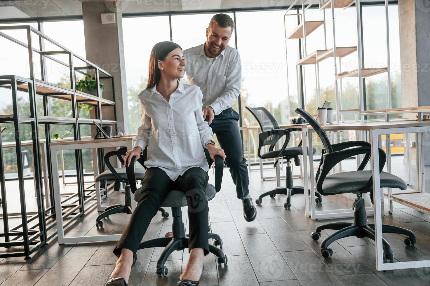 Having fun by riding the chair. Man, and woman are working in the modern office together photo
