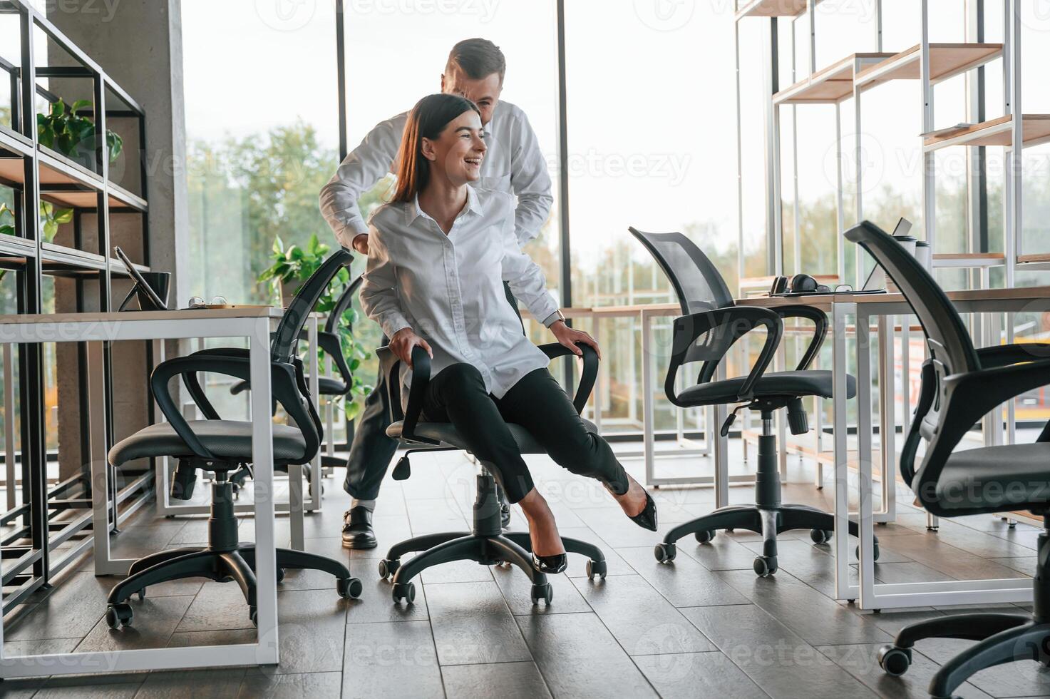 Having fun, by riding the chair. Man and woman are working in the modern office together photo
