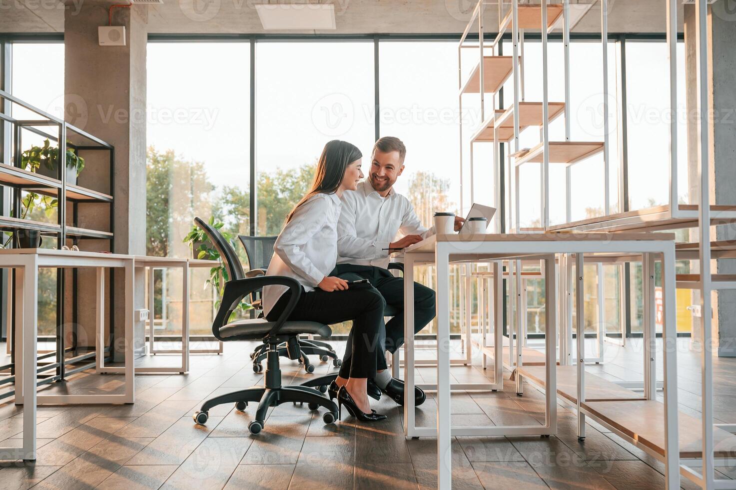 Sitting, by the table with laptop. Man and woman are working in the modern office together photo