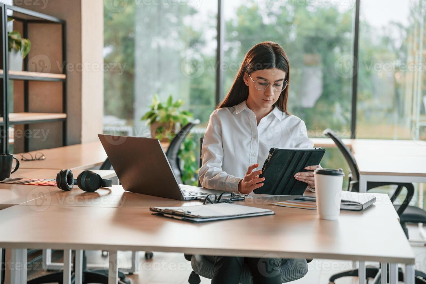 Using ,tablet. Beautiful young woman in white clothes is working in office photo