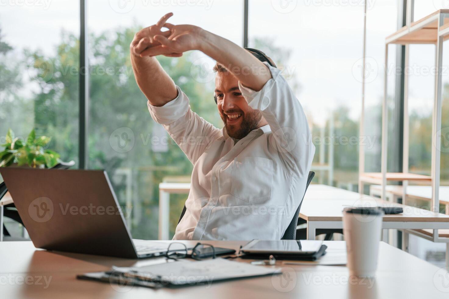 Sitting in headphones by, laptop. Man in formal clothes is working in the modern office photo