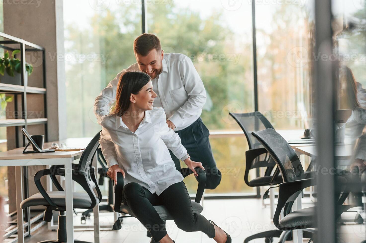 Break time. .Having fun. Riding a chair. Man and woman are working in the modern office together photo