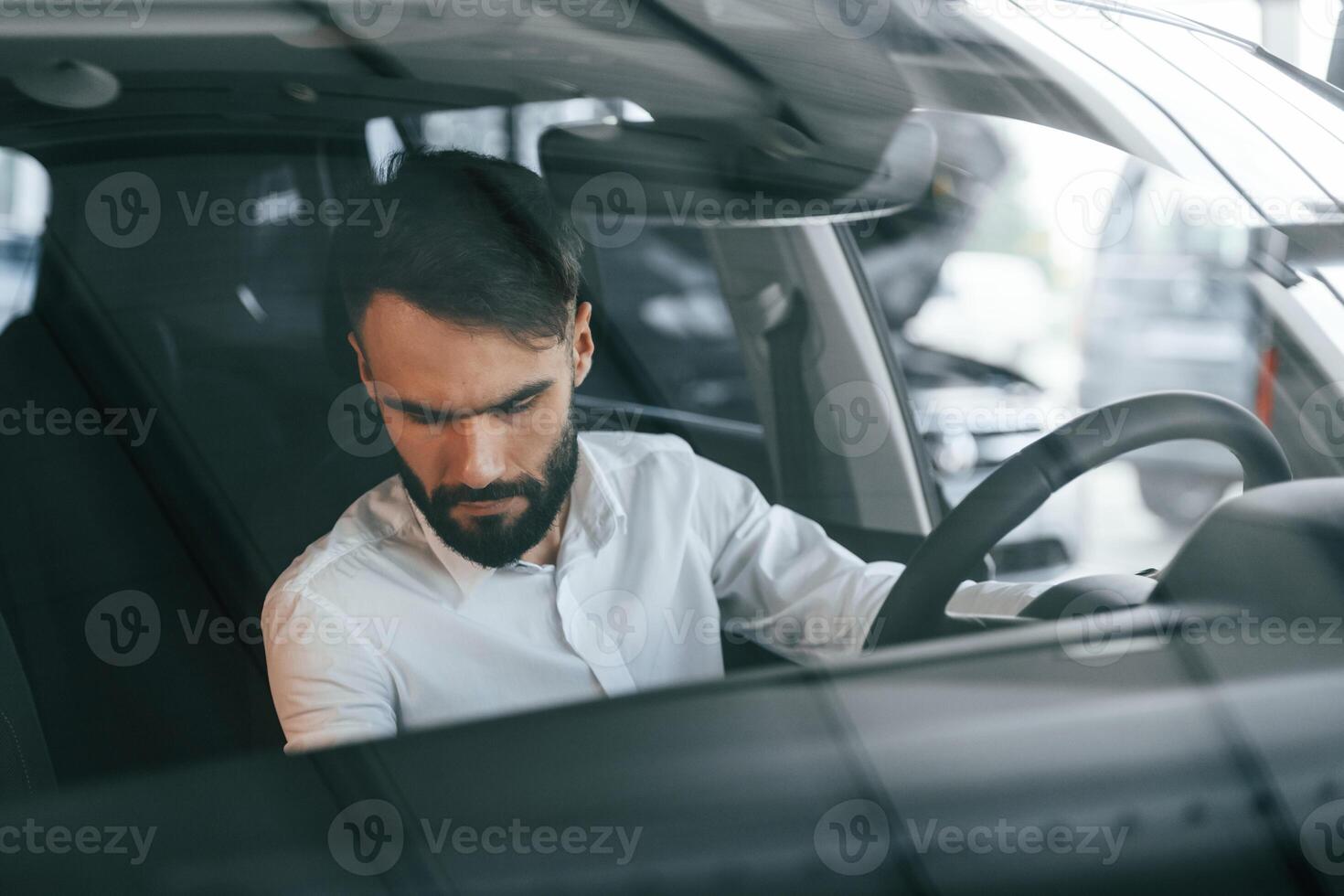Inside, of ,the automobile. Young man in white clothes is in the car dealership photo