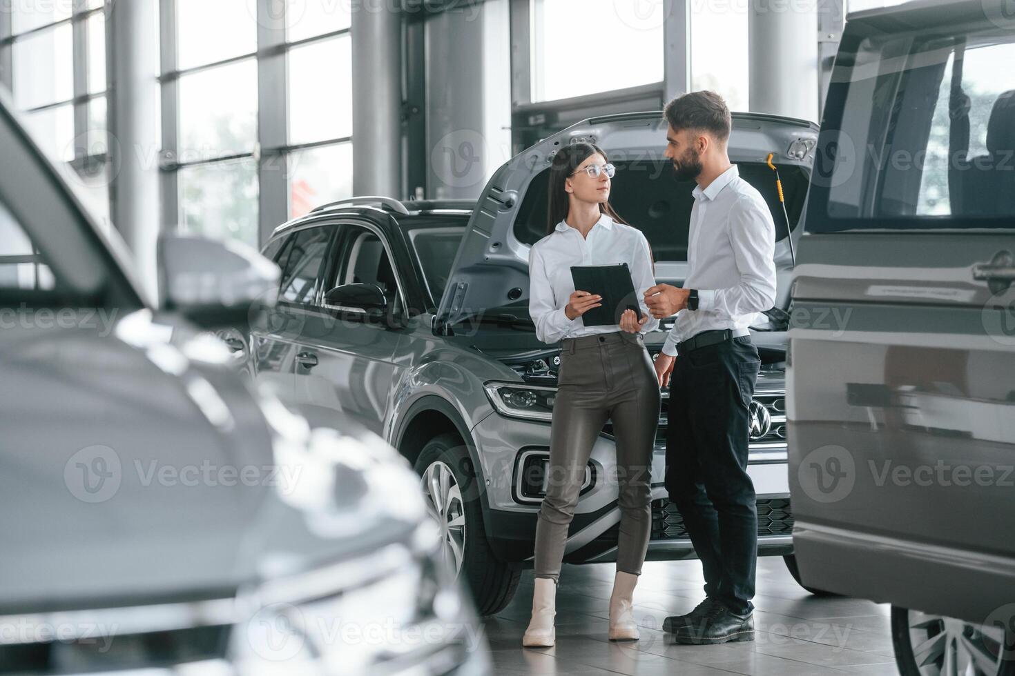Reading information by using tablet.. Man with woman in white clothes are in the car dealership together photo