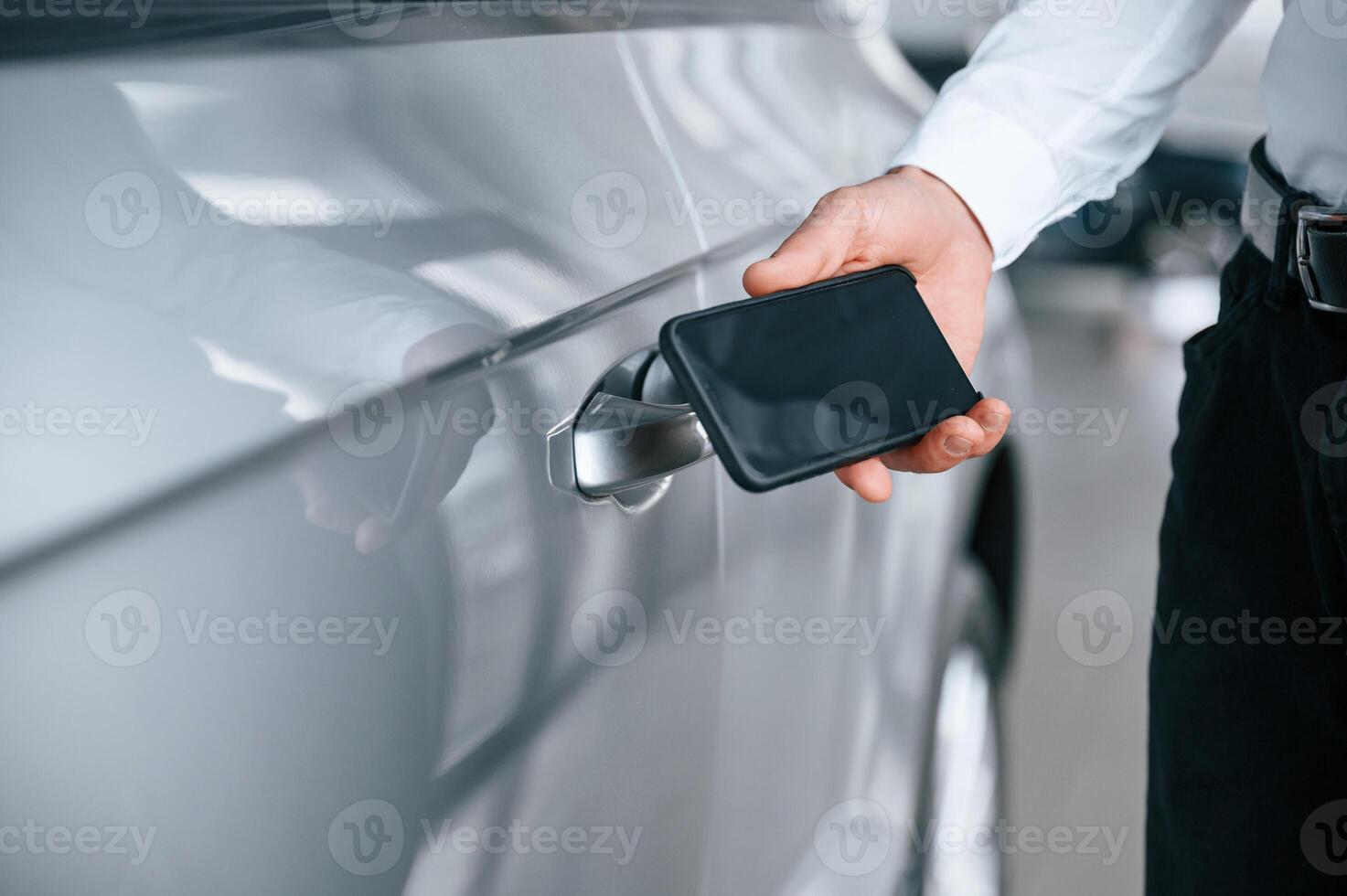 Wit,h smartphone in hand. Young man in white clothes is in the car dealership photo
