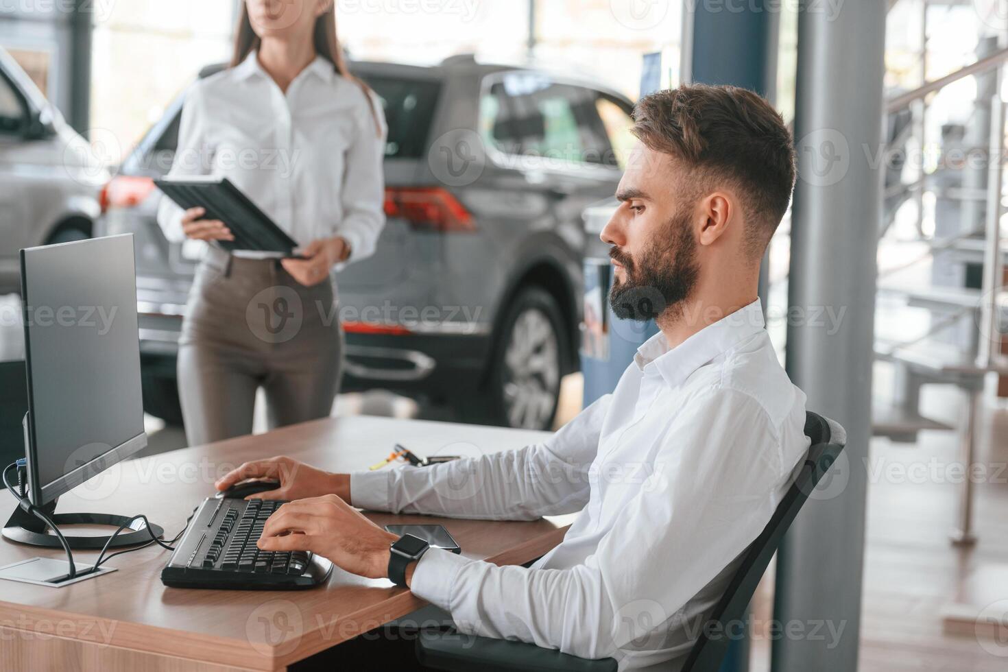 Sitting by, table and working. Man with woman in white clothes are in the car dealership together photo
