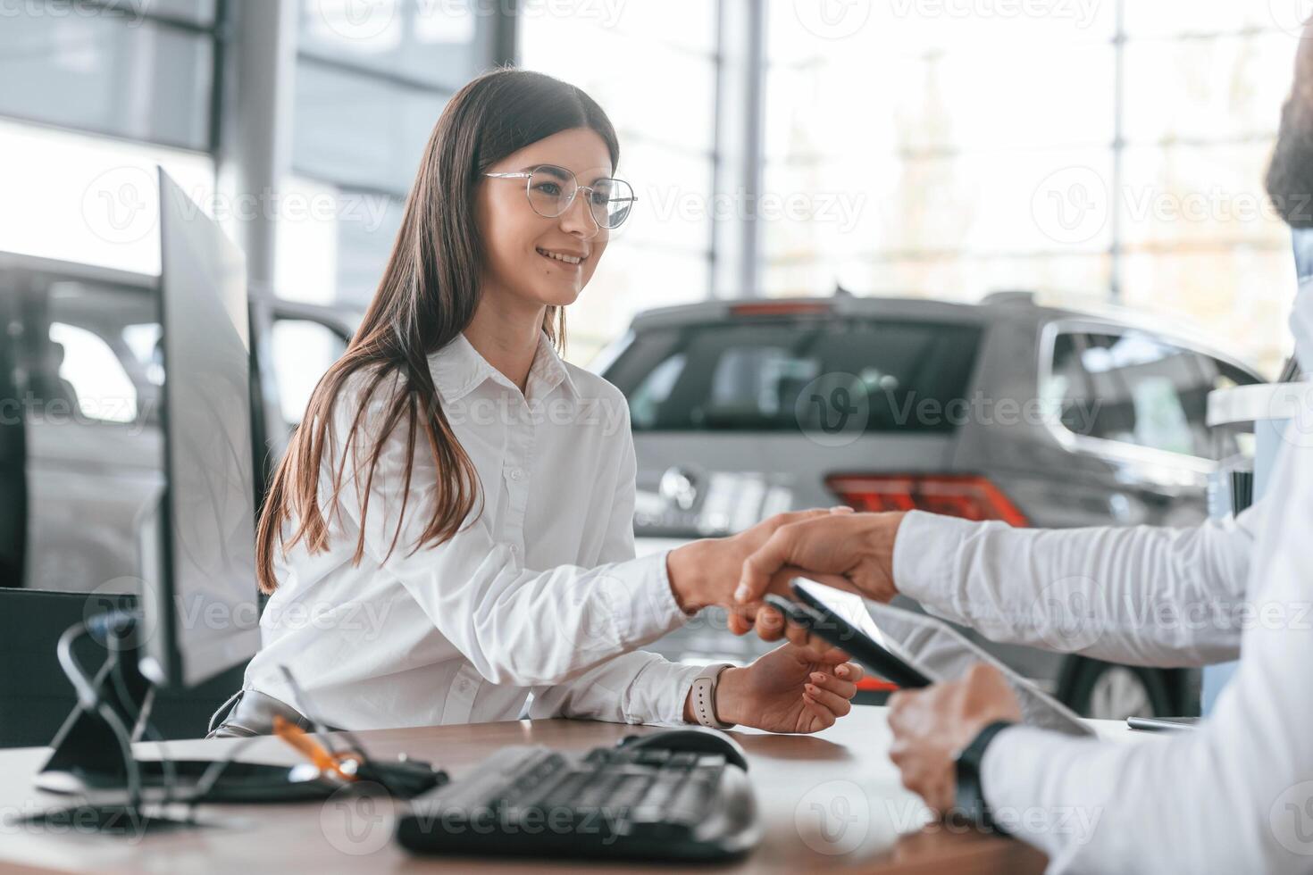 Successful, deal. Sitting and doing handshake. Man with woman in white clothes are in the car dealership together photo