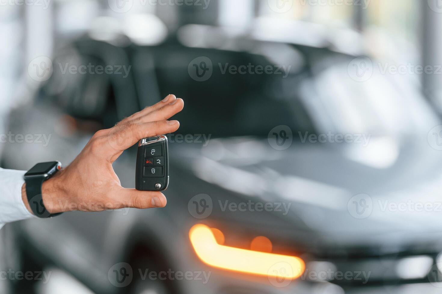 Using the keys ,remote controller. Young man in white clothes is in the car dealership photo