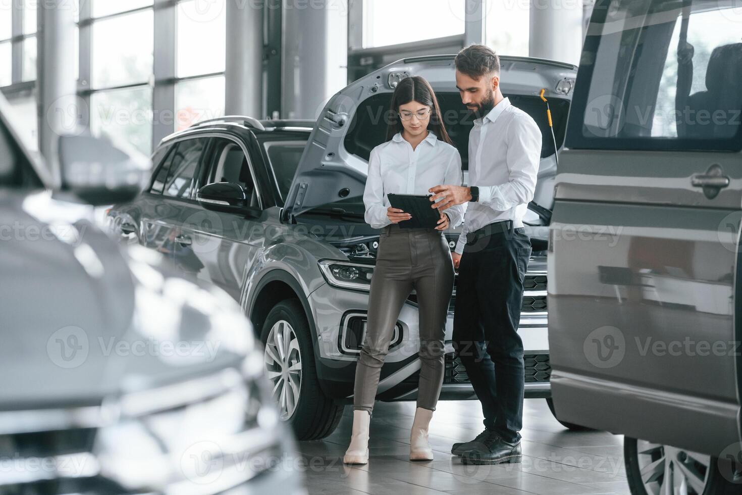 Reading information ,by using tablet.. Man with woman in white clothes are in the car dealership together photo