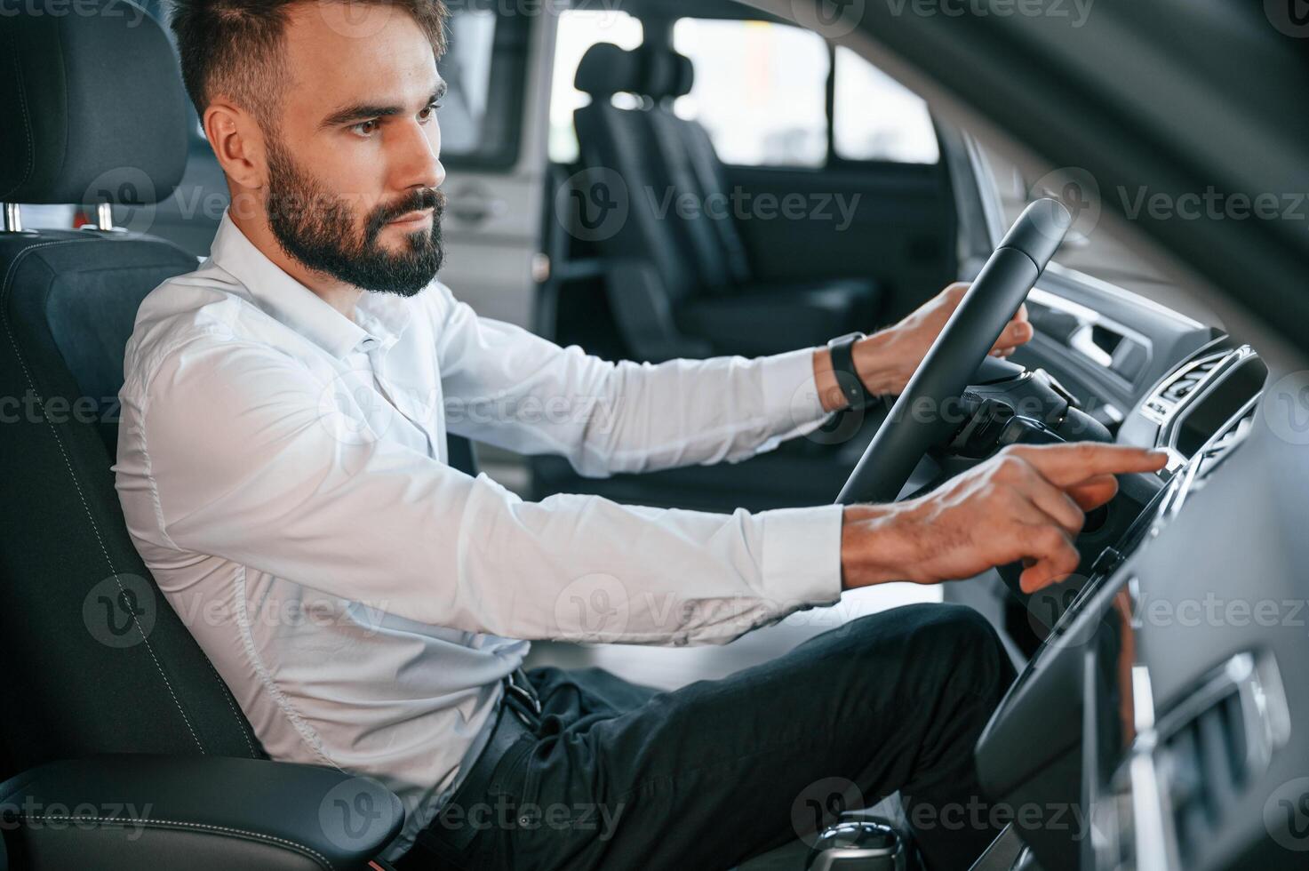 Side view.. Sitting inside of a automobile. Young man in white clothes is in the car dealership photo