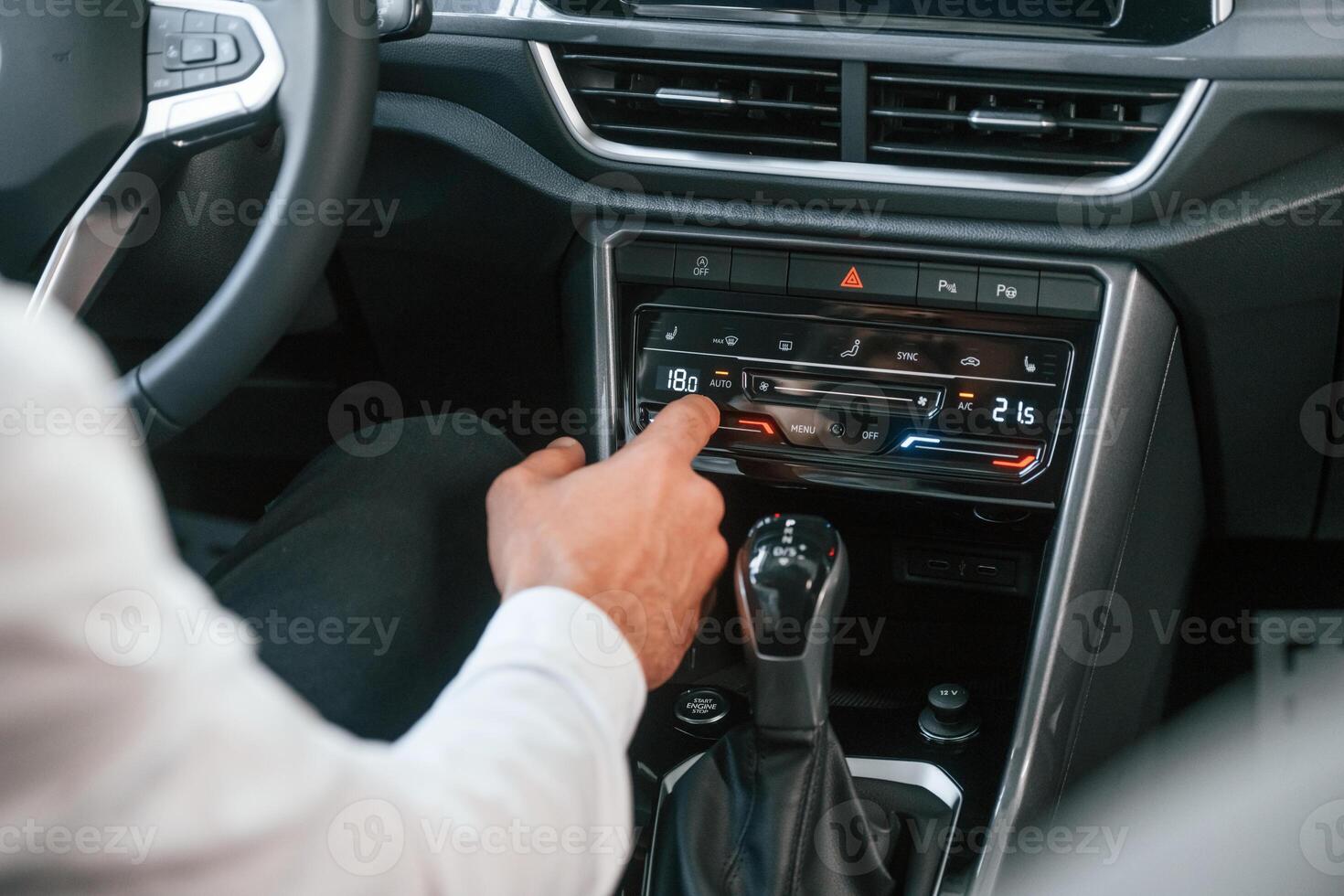 Using the radio. Young man in white clothes is in the car dealership photo