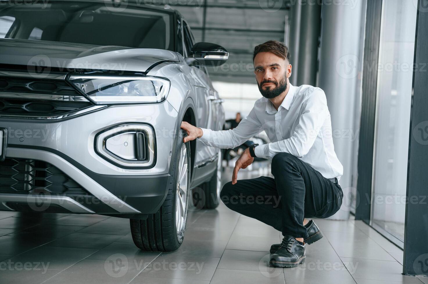 Checking the tires. Young ,man in white clothes is in the car dealership photo