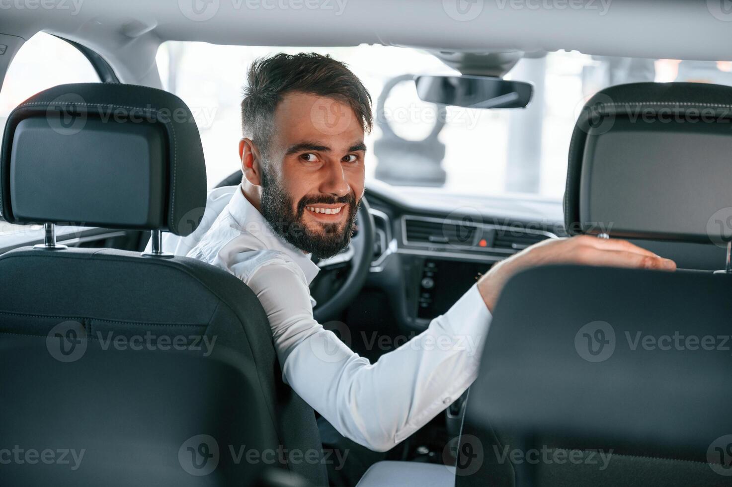 Looking, behind. Young man in white clothes is in the car dealership photo