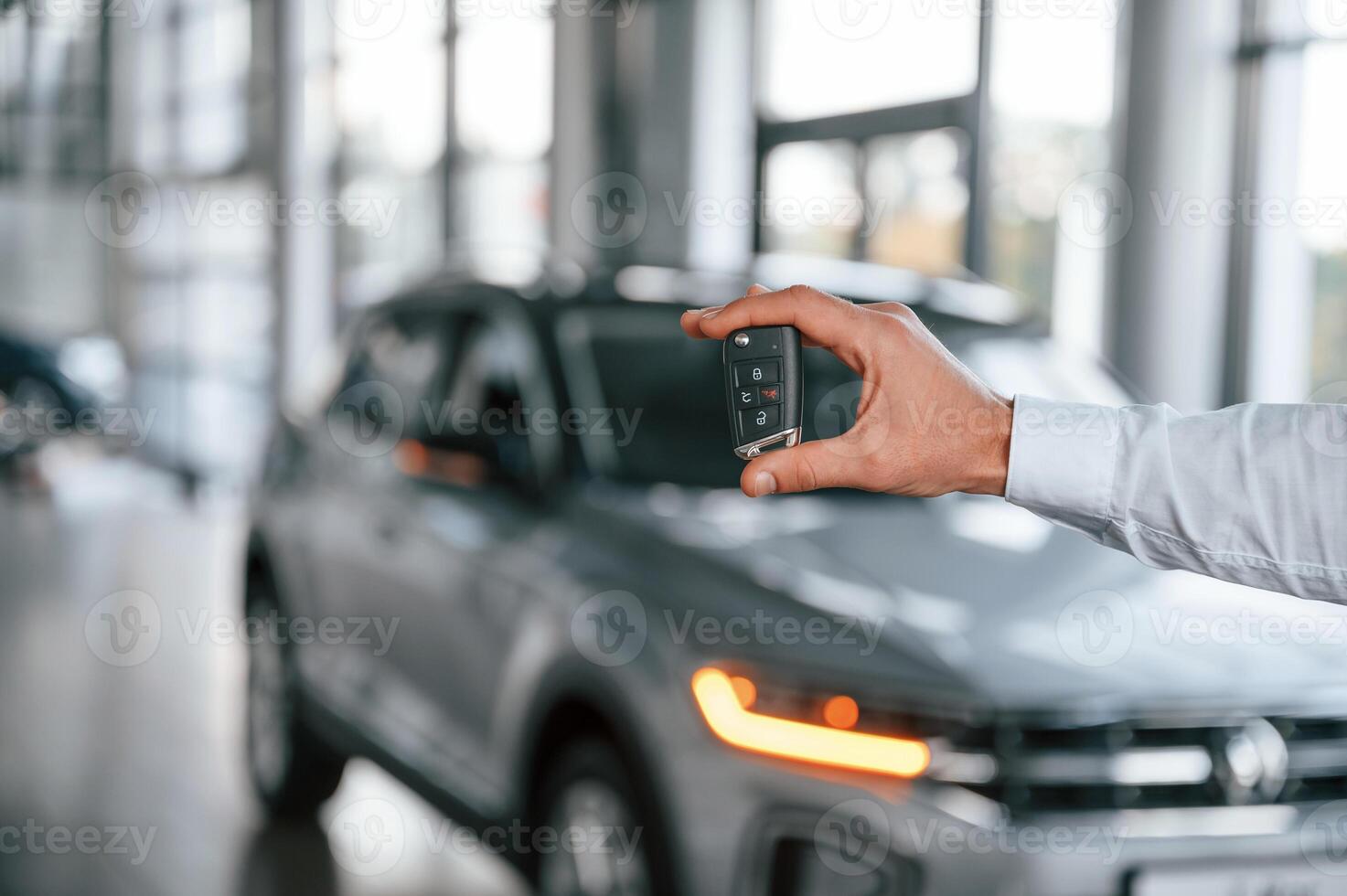 Closing ,the automobile by remote keys. Young man in white clothes is in the car dealership photo