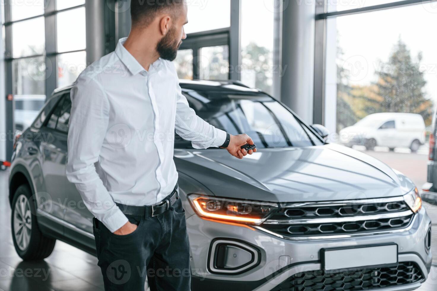 Closing the, automobile by remote keys. Young man in white clothes is in the car dealership photo