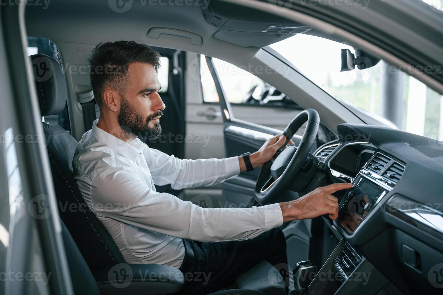 Examining, the salon of the automobile. Young man in white clothes is in the car dealership photo