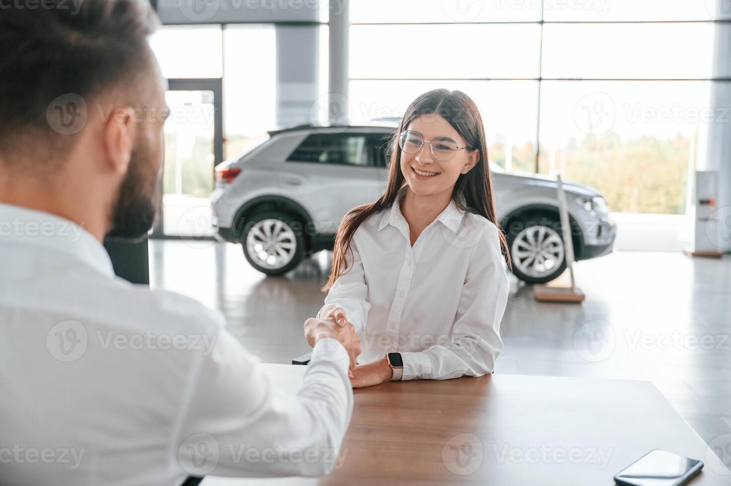 Cheerful customer is ,smiling. Man with woman in white clothes are in the car dealership together photo