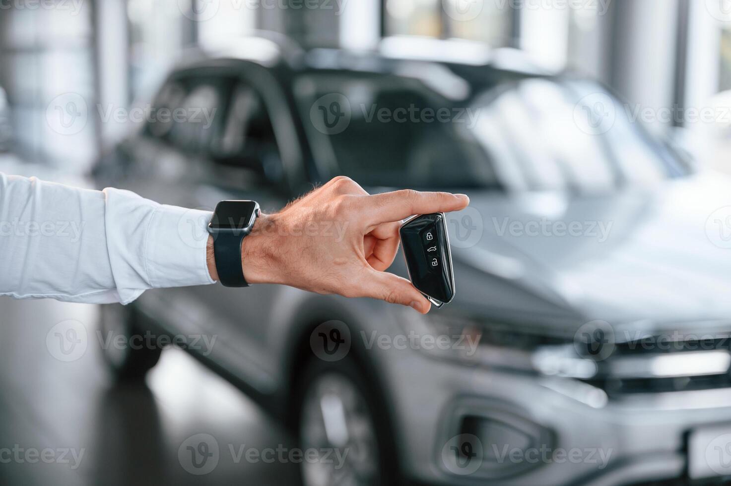 Close up view of keys that are in hand. Young man ,in white clothes is in the car dealership photo