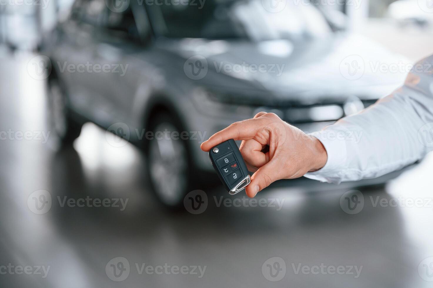 Close ,up view of keys that are, in hand. Young man in white clothes is in the car dealership photo