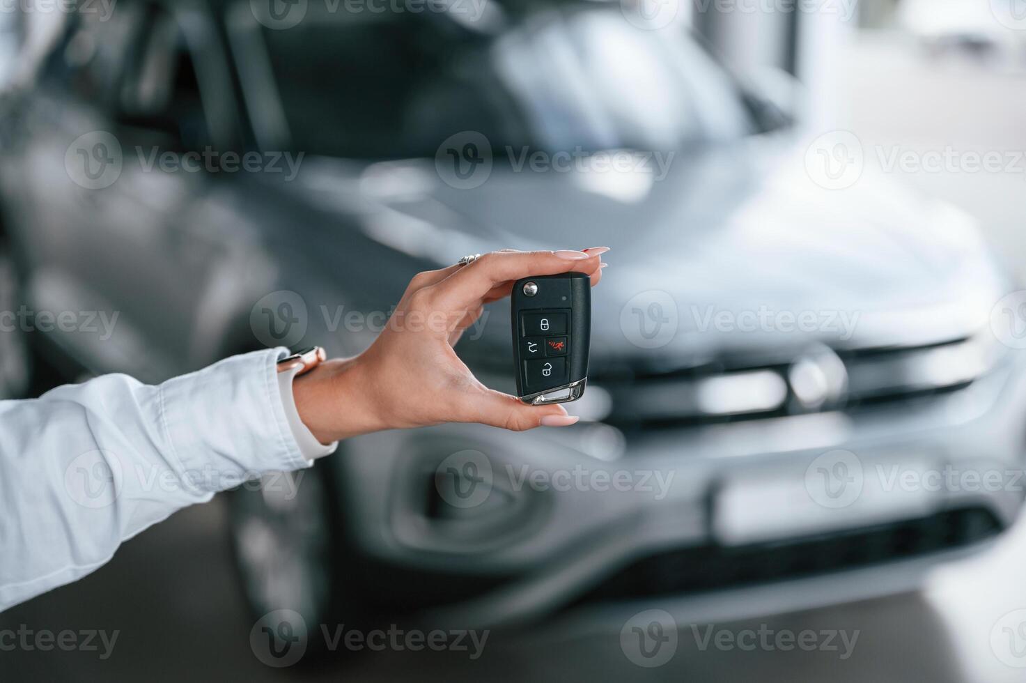 New owner, holding keys. Young woman in white formal clothes is in the at dealership photo