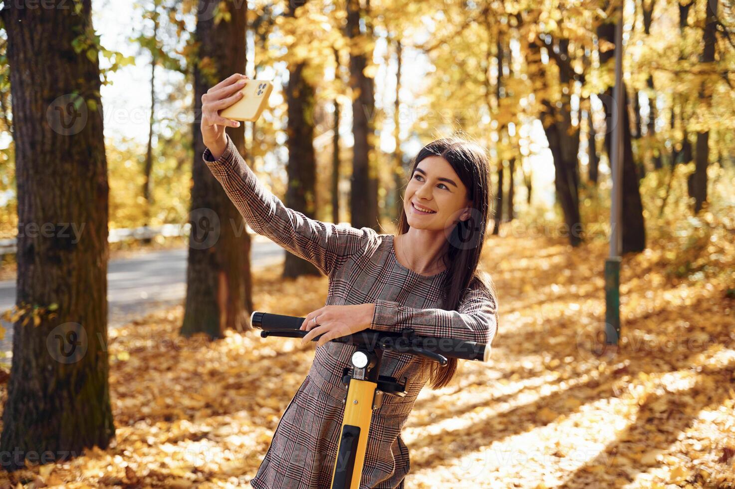 Young woman is making selfie by using smartphone while standing on the electric scooter photo