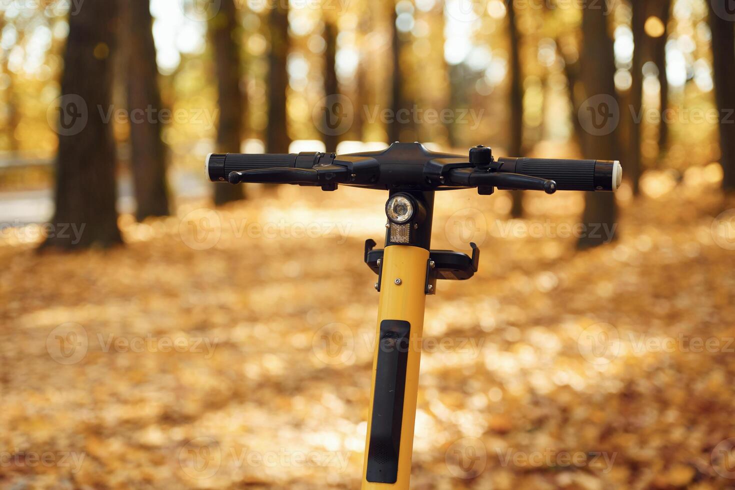 Yellow electric scooter is parked in the forest ,at daytime. Autumn season photo
