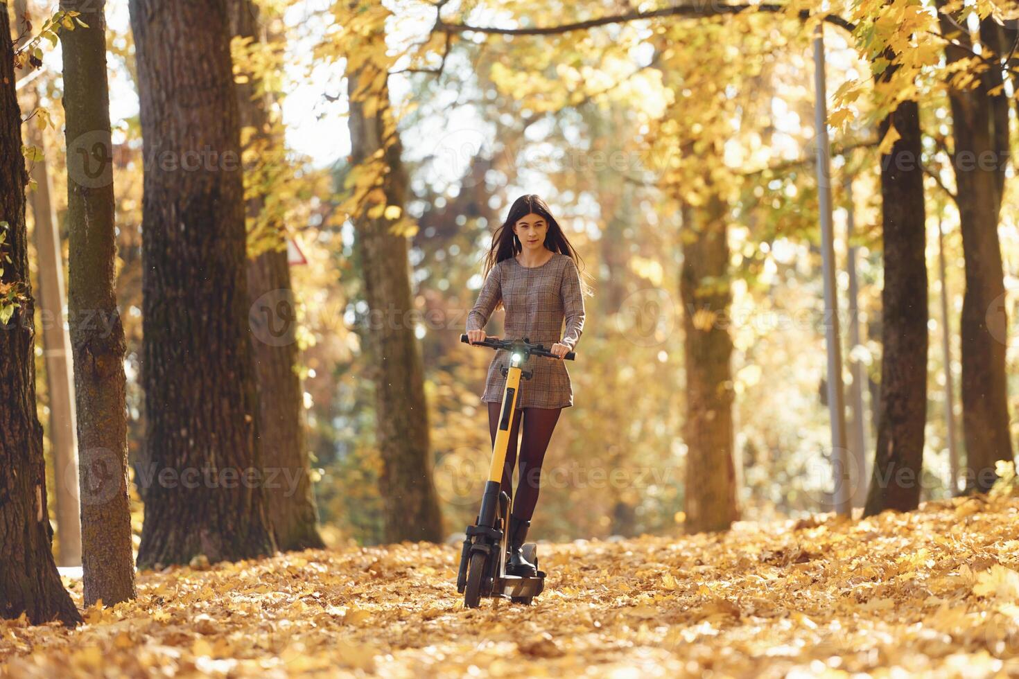 Front, view. Young, woman is riding electric scooter in the autumn forest photo