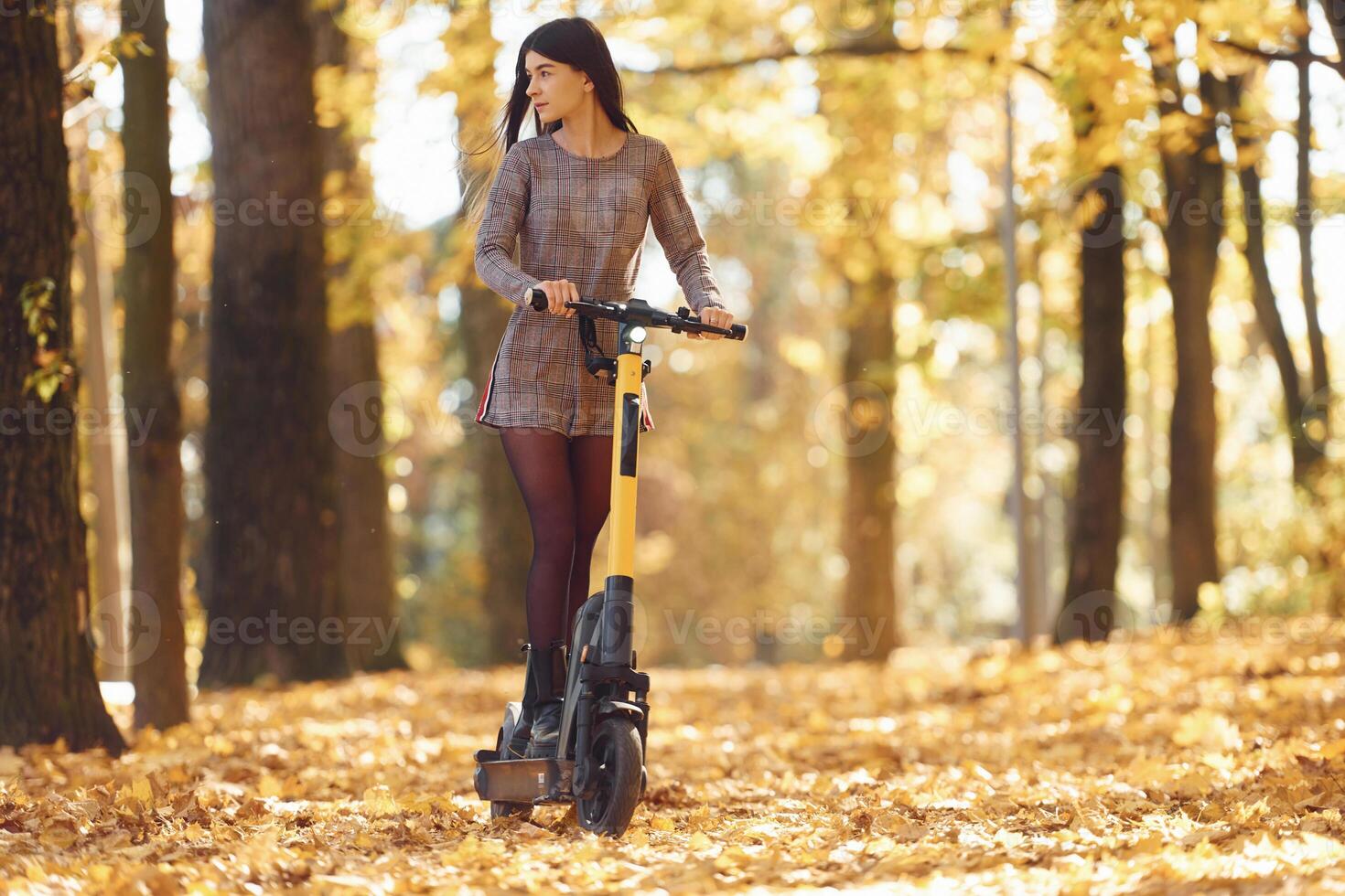 Front view.. Young woman is riding electric scooter in the autumn forest photo