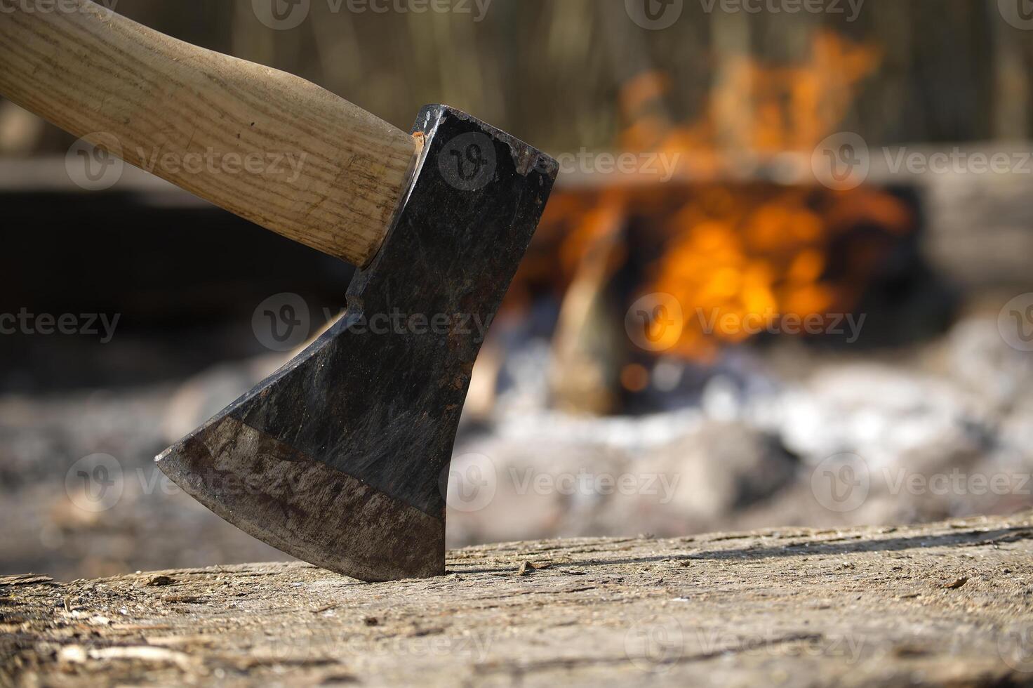A sharp axe stands ready to chop logs next to a warm and inviting campfire in the woods. photo