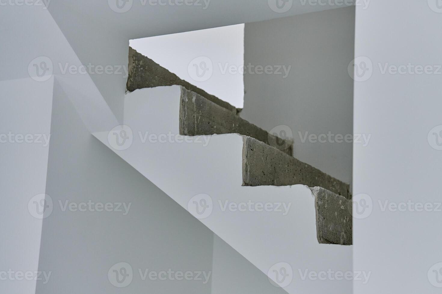 Unfinished concrete staircase in modern minimalist interior. New apartment with raw construction elements and white walls. Building under repair photo