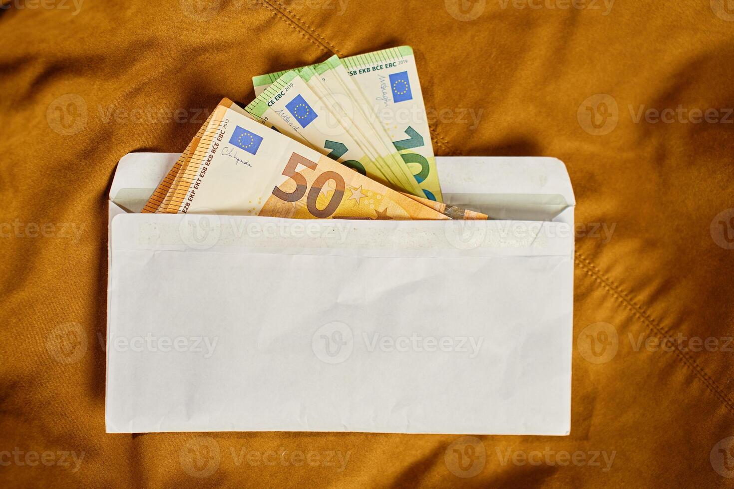Euro banknotes inside white envelope, top view. Close up of cash money on brown background. Concept of corruption, bribery, and hidden cash payments photo