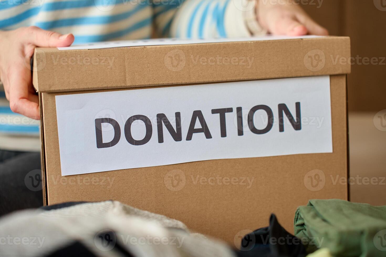 Woman holds donation box filled with clothes on bed, organizing items for charity photo