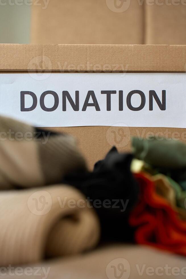 Used clothes near cardboard box labeled Donation at home photo