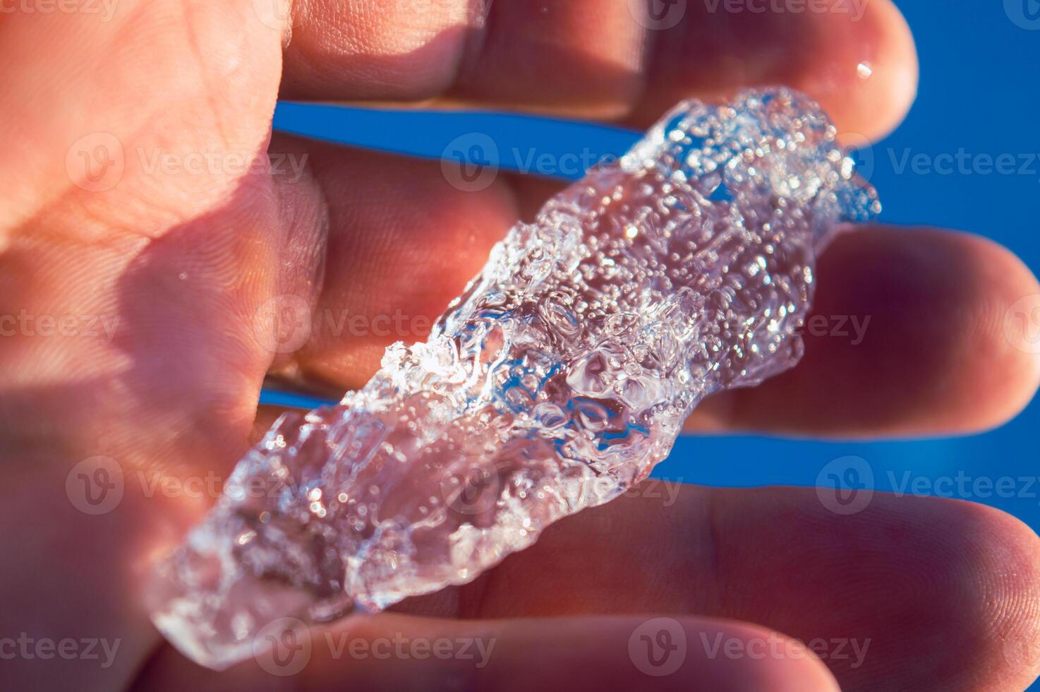 The large transparent crystal of ice in the human hand is seen in the sun's rays. Inside the crystal of interspersed and even rows of bubbles. Beautiful photos of crystalline objects. High quality