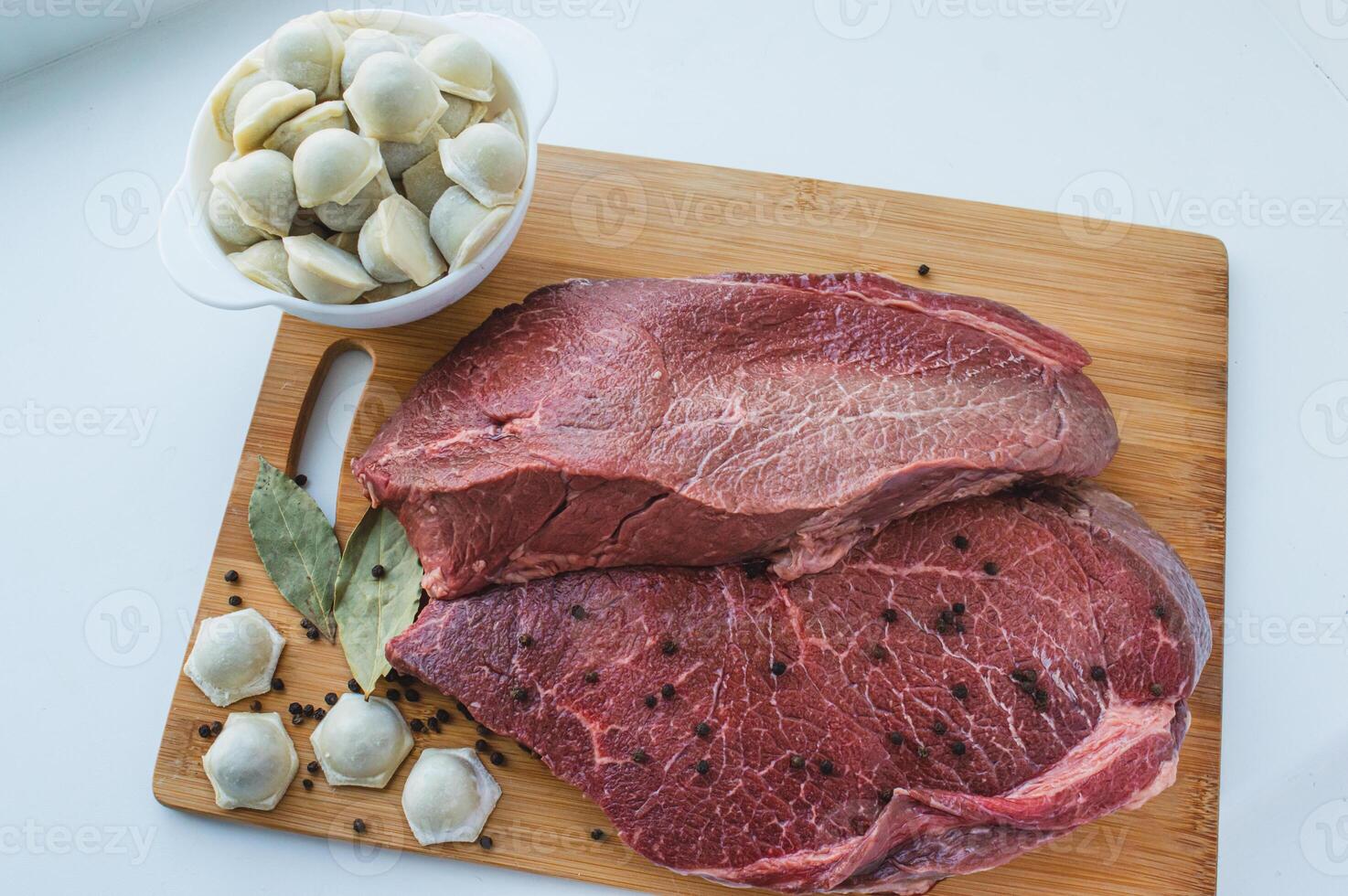A piece of beef meat and beef dumplings on a kitchen board. A banner with meat products marbled beef peppercorns and bay leaves. High quality photo