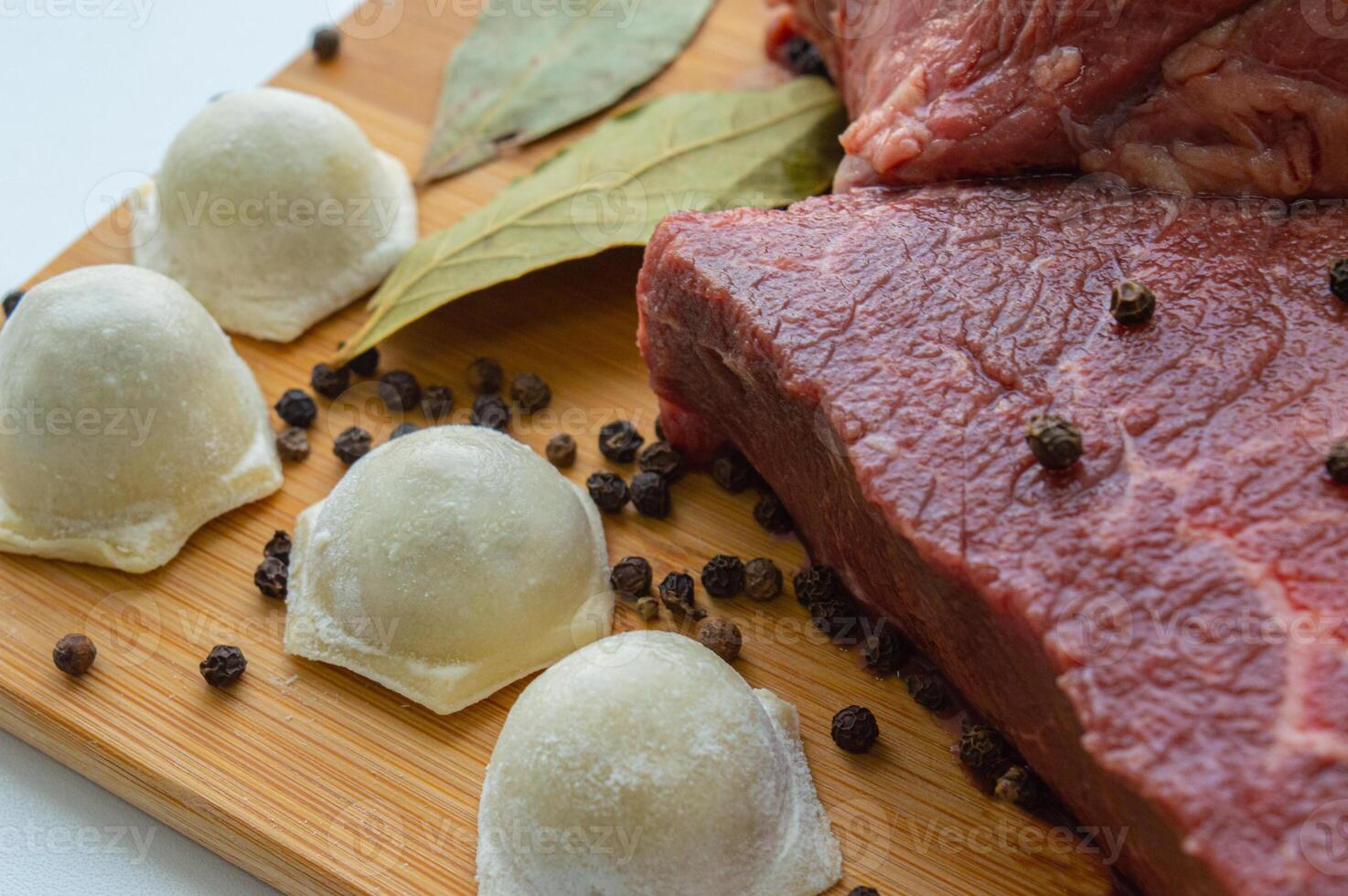 A piece of beef meat and beef dumplings on a kitchen board. A banner with meat products marbled beef peppercorns and bay leaves. High quality photo
