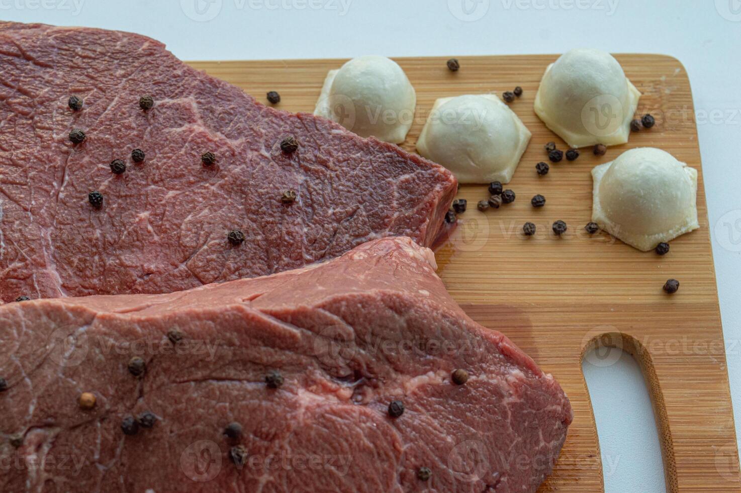 A piece of beef meat and beef dumplings on a kitchen board. A banner with meat products marbled beef peppercorns and bay leaves. High quality photo