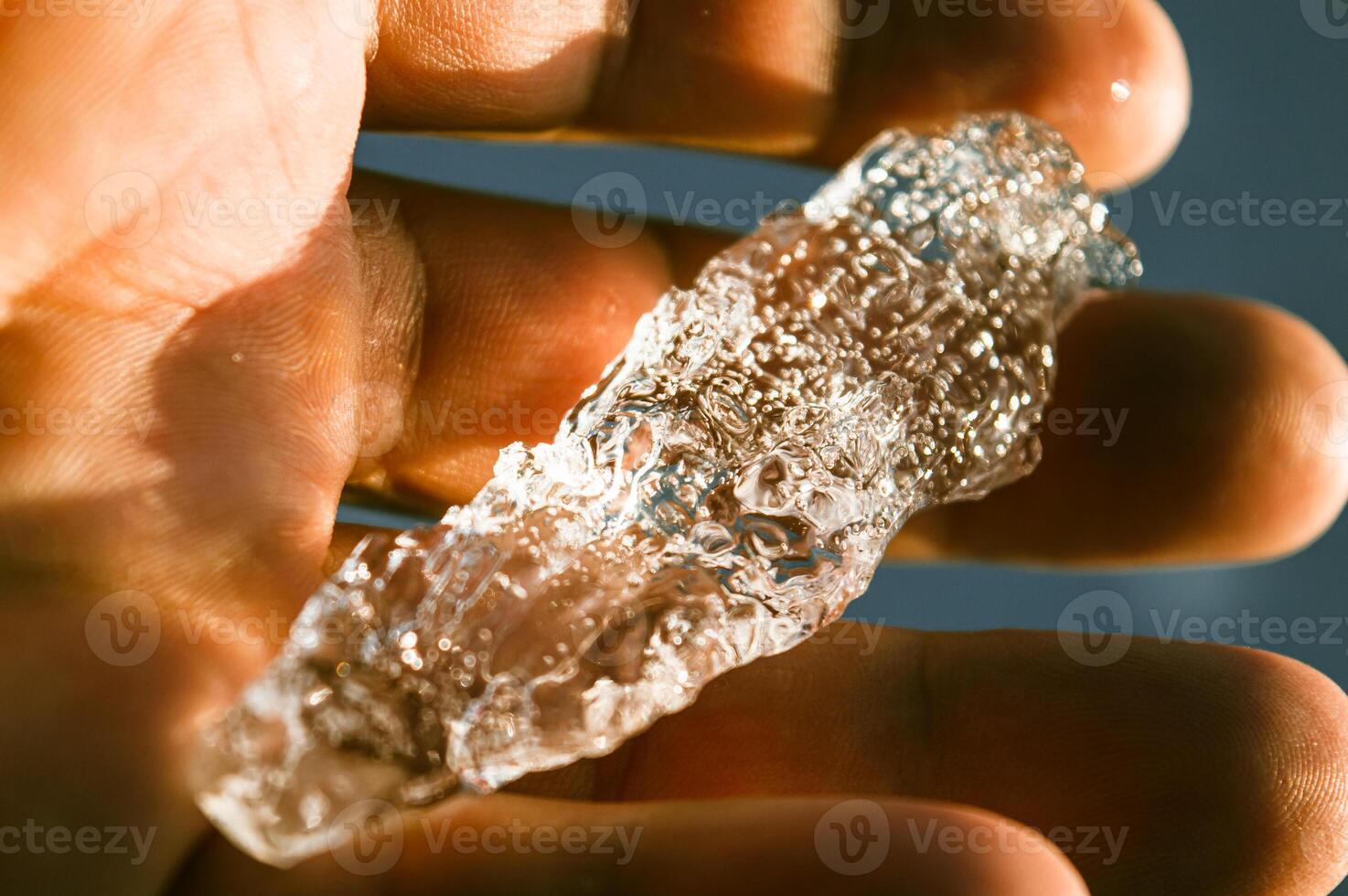 The large transparent crystal of ice in the human hand is seen in the sun's rays. Inside the crystal of interspersed and even rows of bubbles. Beautiful photos of crystalline objects. High quality