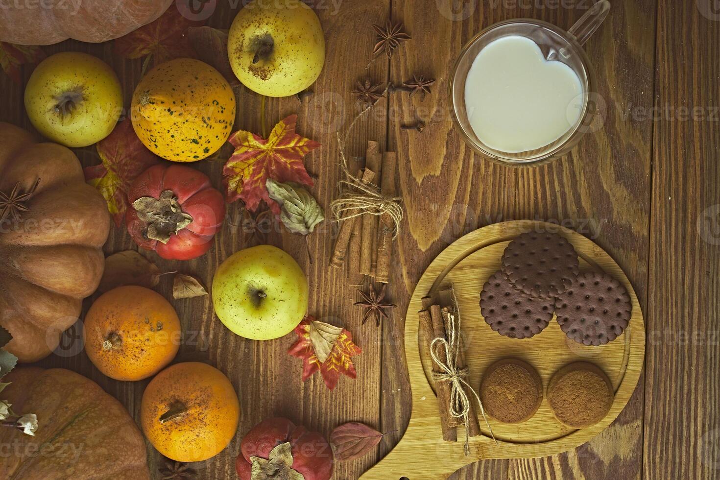 Cookies with milk on the table. Chocolate cookies and cinnamon on the wooden plate with a glass of milk and pumpkin with apple. photo
