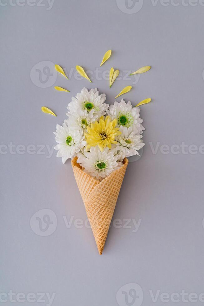 White and yellow flowers and petals in ice cream cone on grey background. Creative spring and summer concept. Flowers aesthetic. Flat lay style. photo