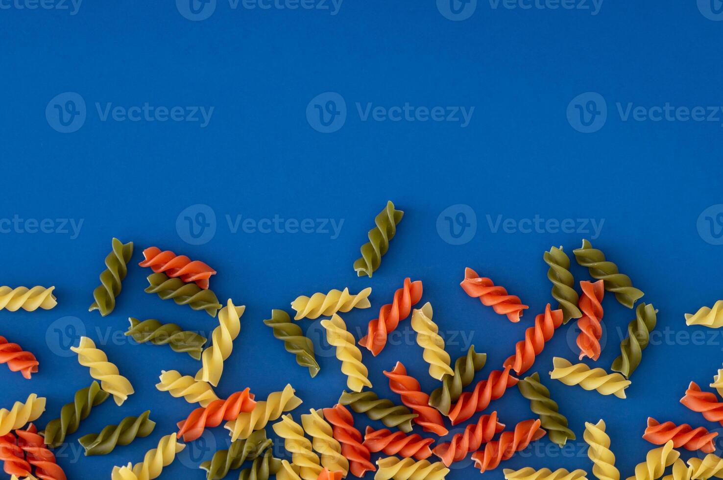 Colorful food layout with natural multicoloured fusilli on blue background with copy space. Minimal pasta concept. Creative food pattern backdrop. Pasta aesthetic. Flat lay style. Top view banner. photo