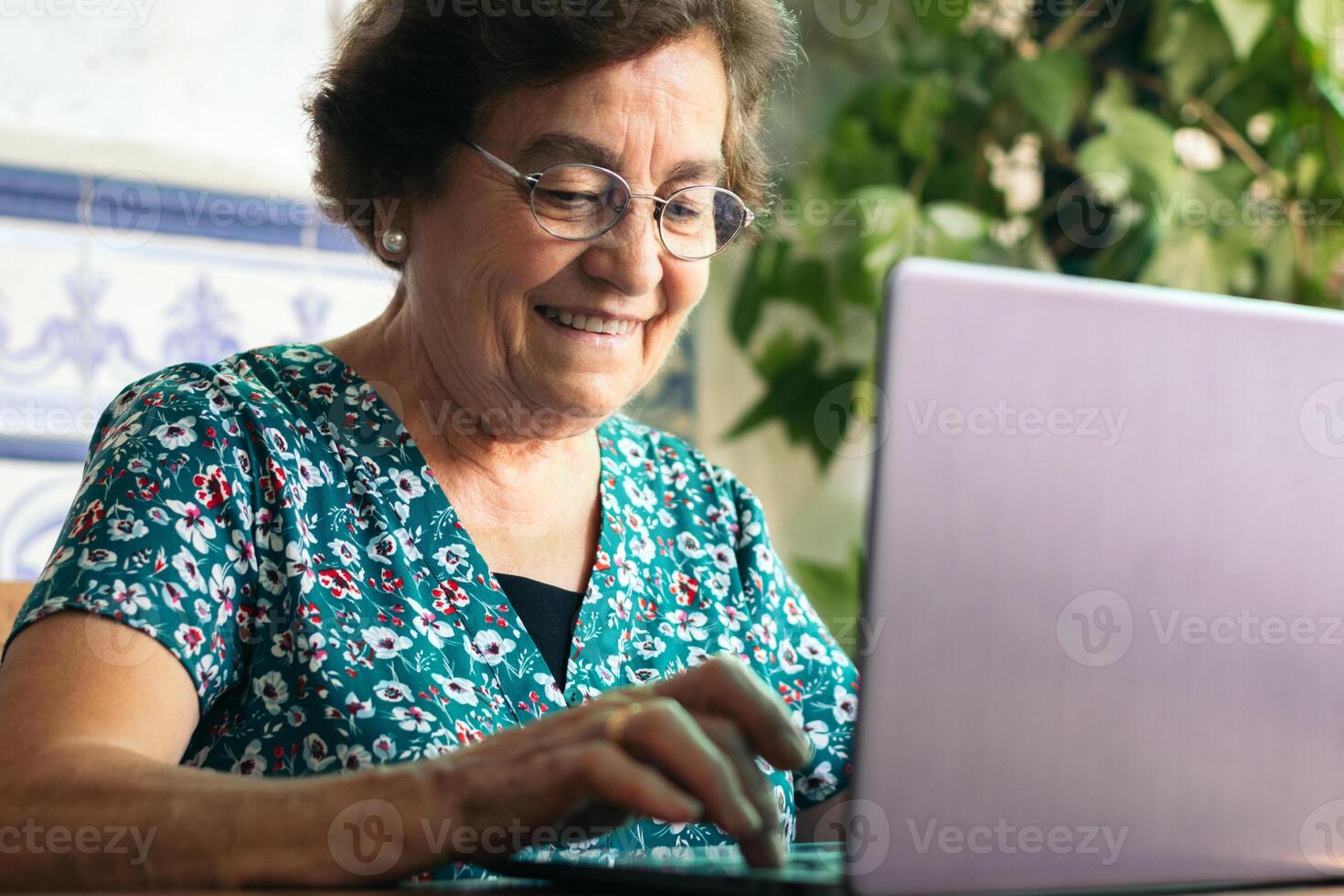 Senior woman with glasses using a laptop and a notebook at home photo