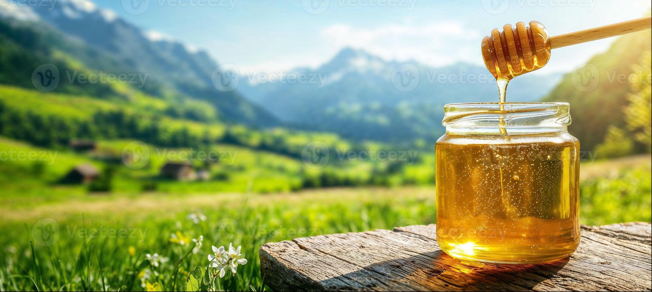 Honey pouring from honey dipper into jar, close-up, sunny landscape with flower meadows, copy space photo